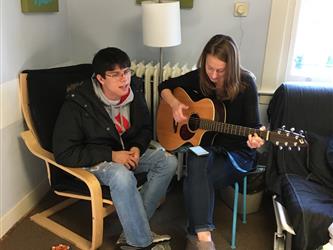 A student playing a guitar for another student